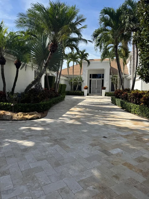 Stone paver entryway bordered by landscaping and palm trees