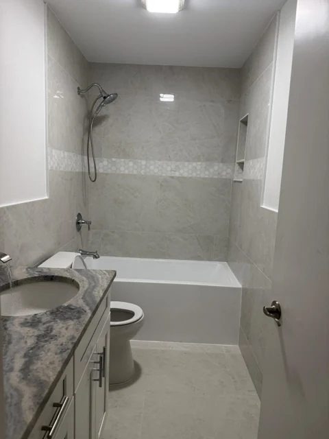 Bathroom with a white bathtub, neutral wall tile, and a stone-topped vanity